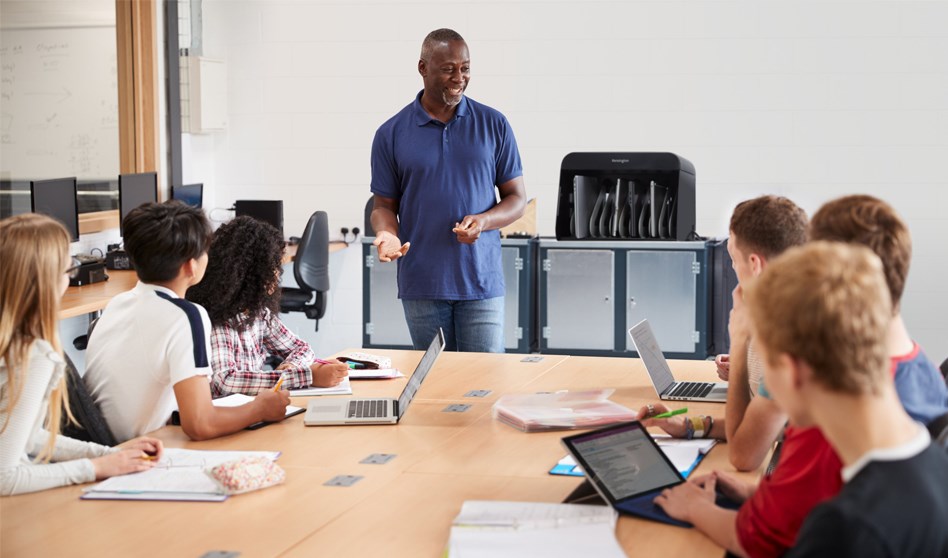 An adult speaking to a teenagers in a classroom with a Kensington Universal AC Charge Station