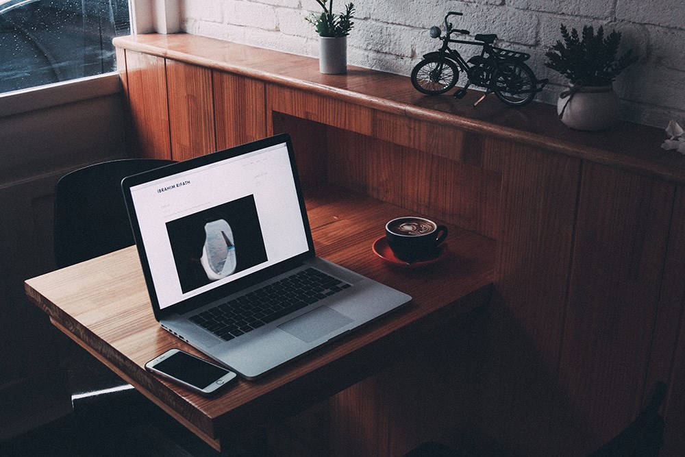 A MacBook set up at a cafe with a latte sitting next to it