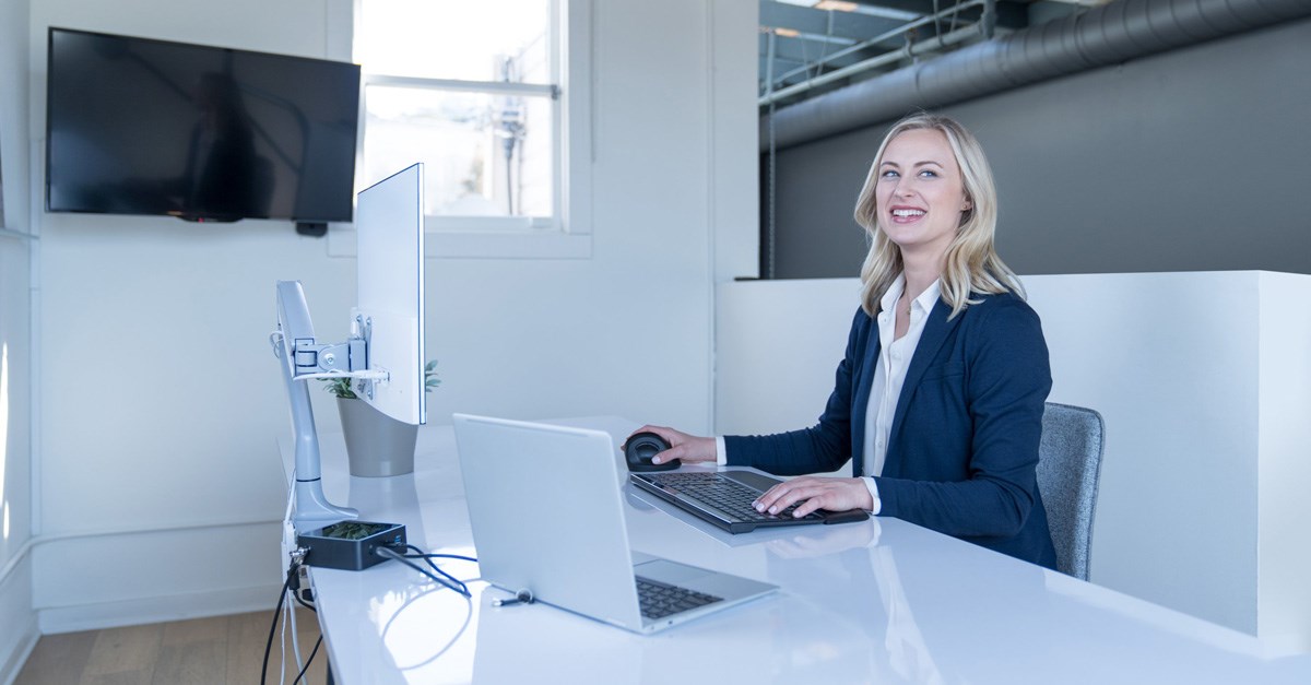 Woman working at a desk setup and using a Kensington vertical mouse and monitor arm