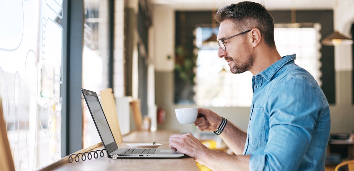 A person working at a coffee shop securing his laptop with a Kensington Lock