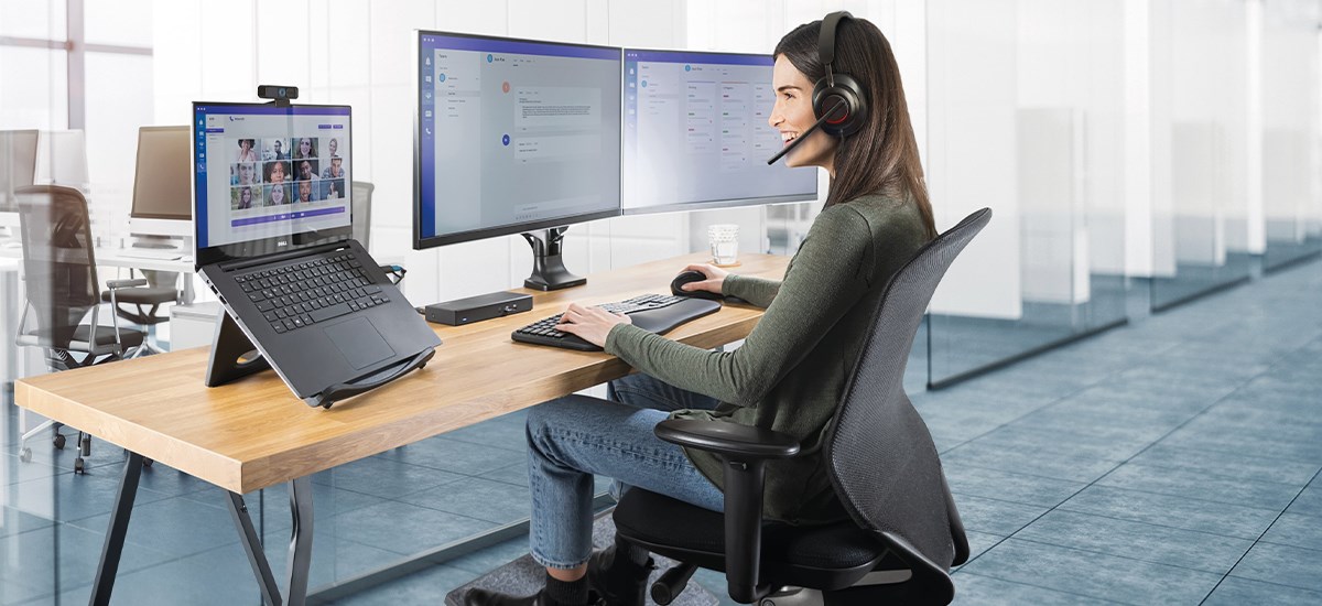 Ergonomic office desk with accessories: keyboard, mouse, laptop riser, docking station and dual monitors.