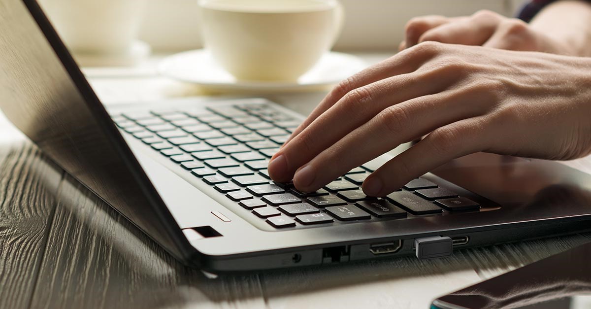 Laptop with a VeriMark Biometric Kensington security key and hands on keyboard. 