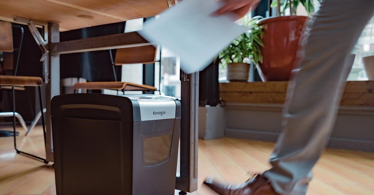 A man is inserting a paper sheet into a Kensington shredder.