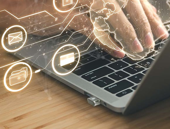 Woman typing on her laptop with a verimark securty key connected to it.