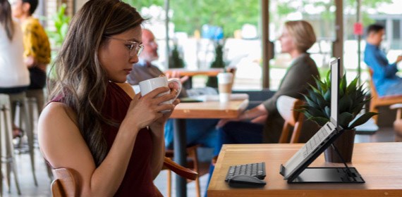 Woman drinking coffee while working on laptop with mouse keyboard laptop riser in coffee shop.